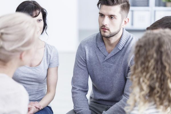 goodencenter-opioid-addiction-photo-of-Unhappy-young-man-sitting-with-other-people-during-addiction-therapy