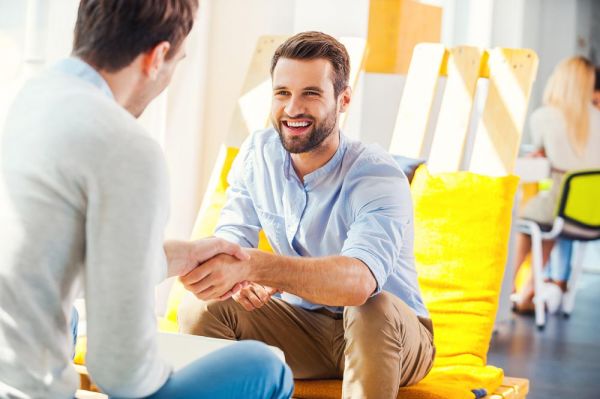 Goodencenter-Why-Employers-Need-to-Talk-About-Mental-Health-in-the-Workplace-photo-of-Sealing-a-deal!-Two-happy-young-men-shaking-hands-while-sitting-in-the-rest-area-of-the-office