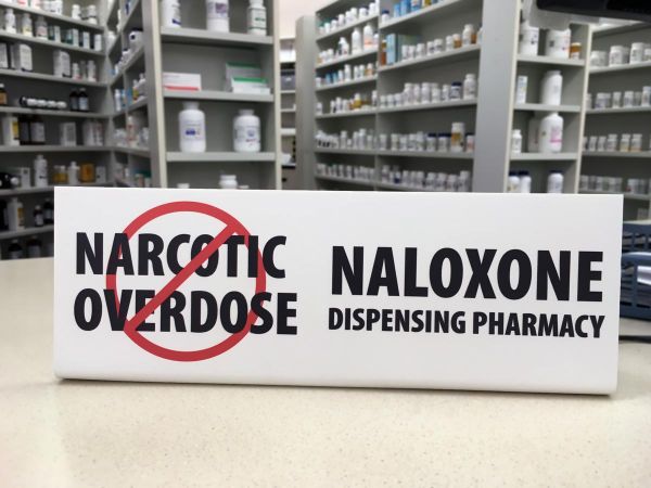 Naloxone pharmacy sign on counter showing the pharmacy now sells over the counter naloxone injections to prevent drug overdose