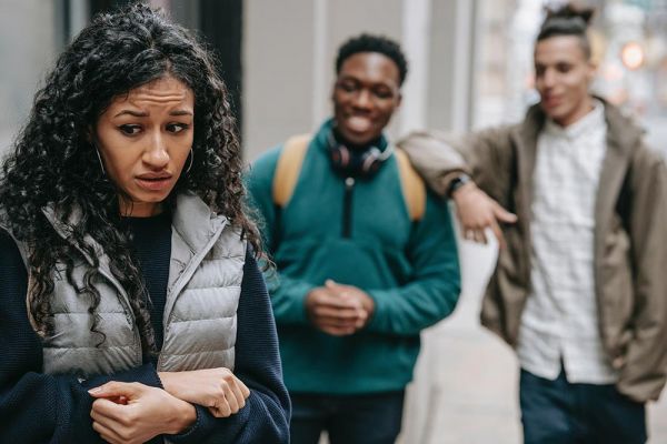 concerned looking young woman being bullied by two young mean standing behind her and laughing