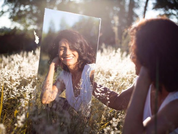 a photo of a woman with mental health disorder sitting on the grass looking at the mirror, narcissism