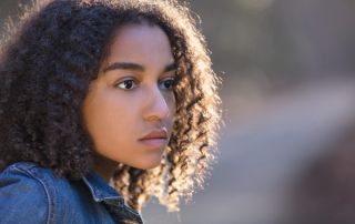 photo of a beautiful mixed race African American girl teenager female young woman outside by a road looking sad depressed or thoughtful