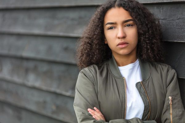 photo of an african-american young woman outside wearing a green bomber jacket looking sad depressed or thoughtful